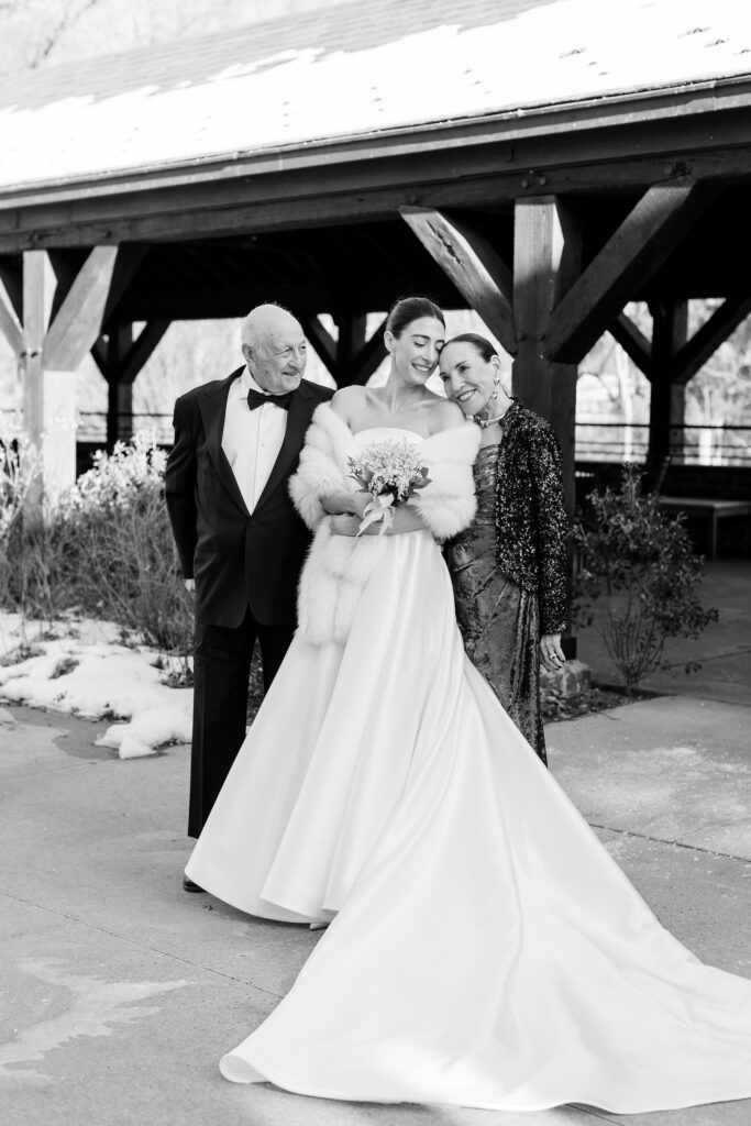 bride and parents posting and smiling outside Blue Hill at Stone Barn with snow on the ground