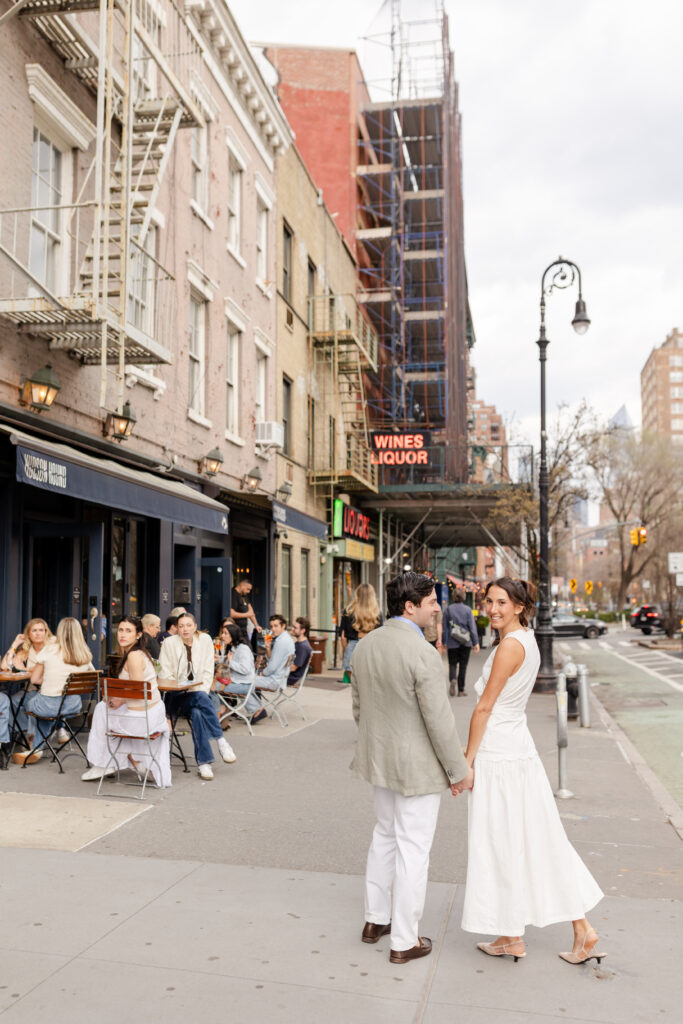 couple holding hands walking down West Village in front of Hudson Hound for their engagement photos