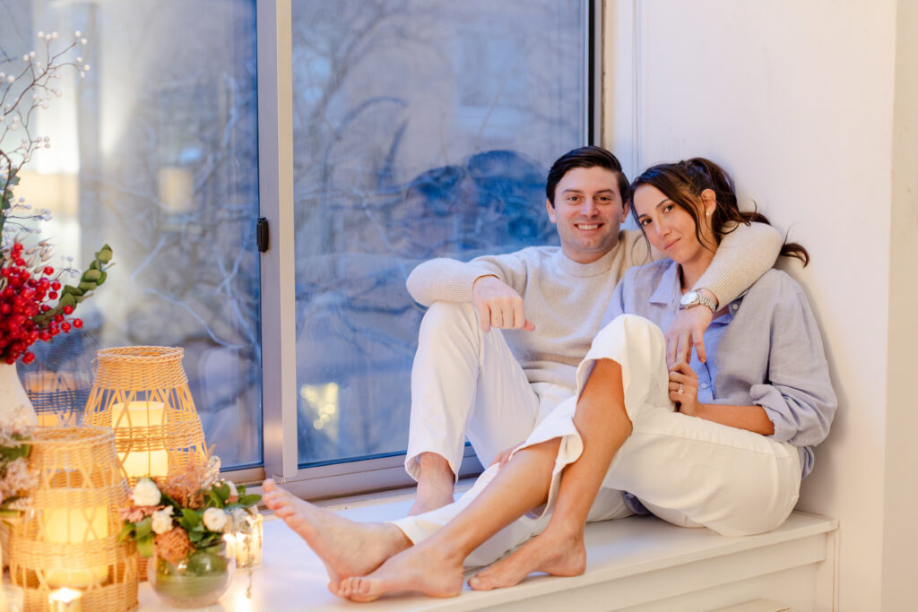 couple cuddling at by window in their apartment during engagement photos, West Village engagement locations at home