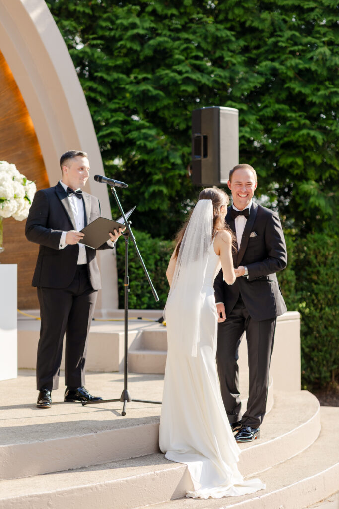 bride and groom laughing during ceremony in front of bandshell at outdoor summer wedding at Westchester Country Club