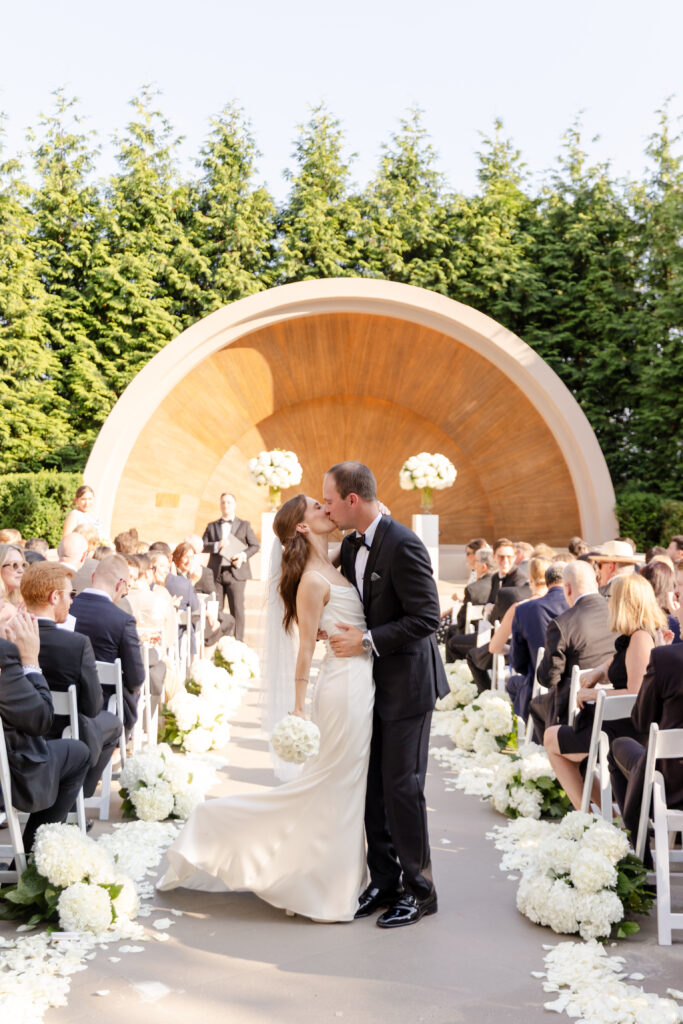 bride and groom kiss down the aisle as newlyweds during their outdoor summer ceremony at Westchester Country Club in front the bandshell