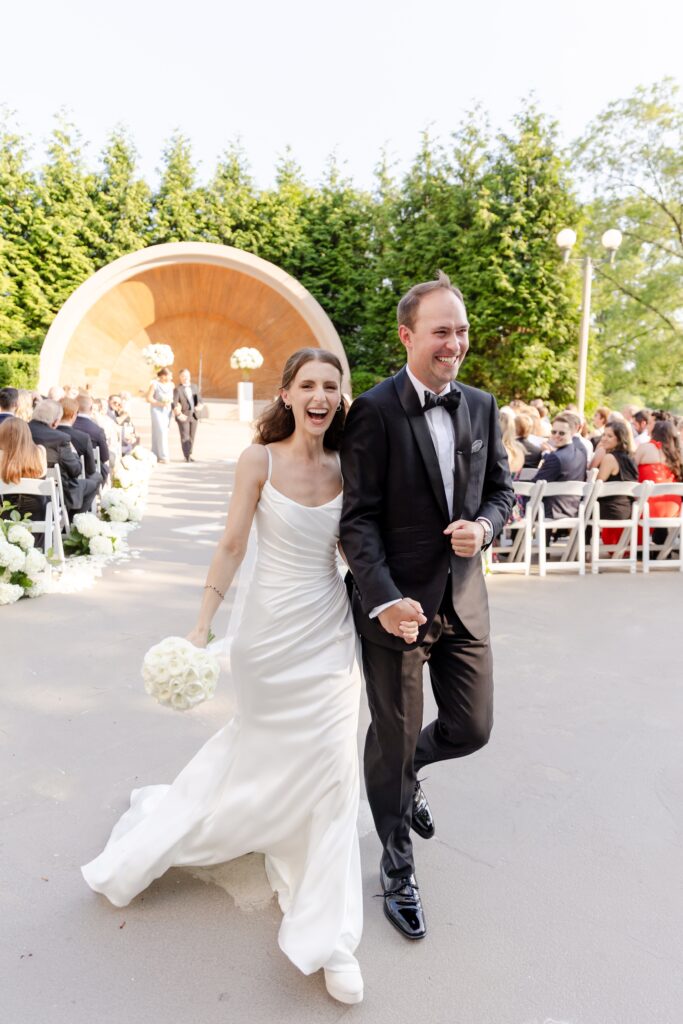 bride and groom smiling holding hands after ceremony and walk down the aisle as a married couple