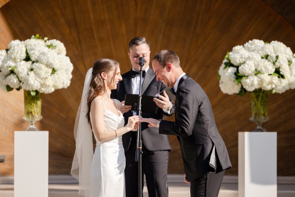 bride and groom exchanging rings during their outdoor summer wedding at Westchester Country Club in front the bandshell