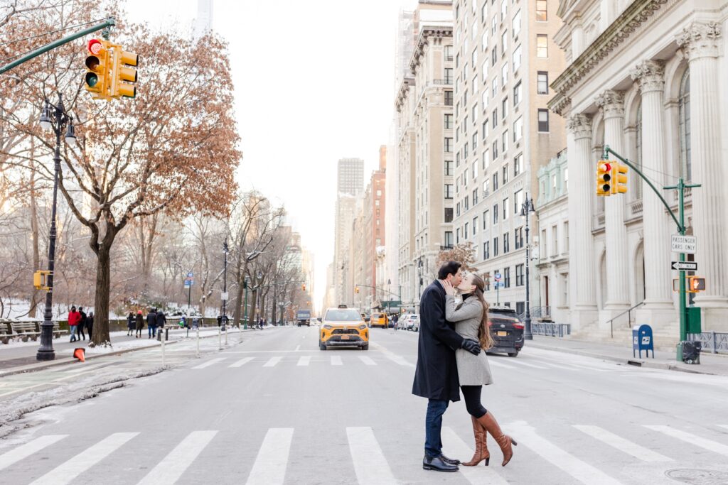 couple kissing in the snowy streets of NYC next to Central Park with yellow taxi in the background, winter engagement session in New York