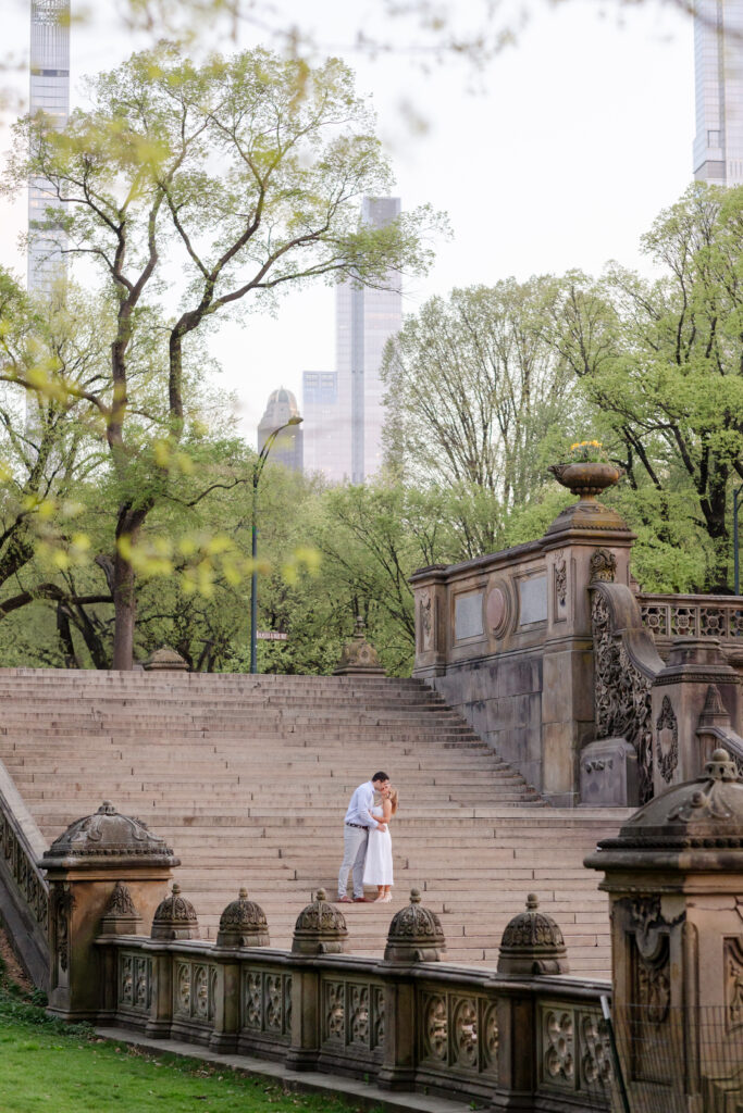 guy holding his fiance on the stairs of the Bethesda Terrace in Central Park, couple embracing during golden hour engagement session in Central Park