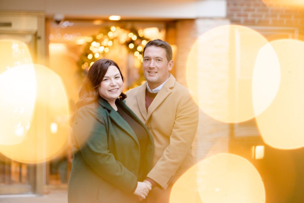 couple surrounded by Christmas lights holding hands during winter engagement session in New York