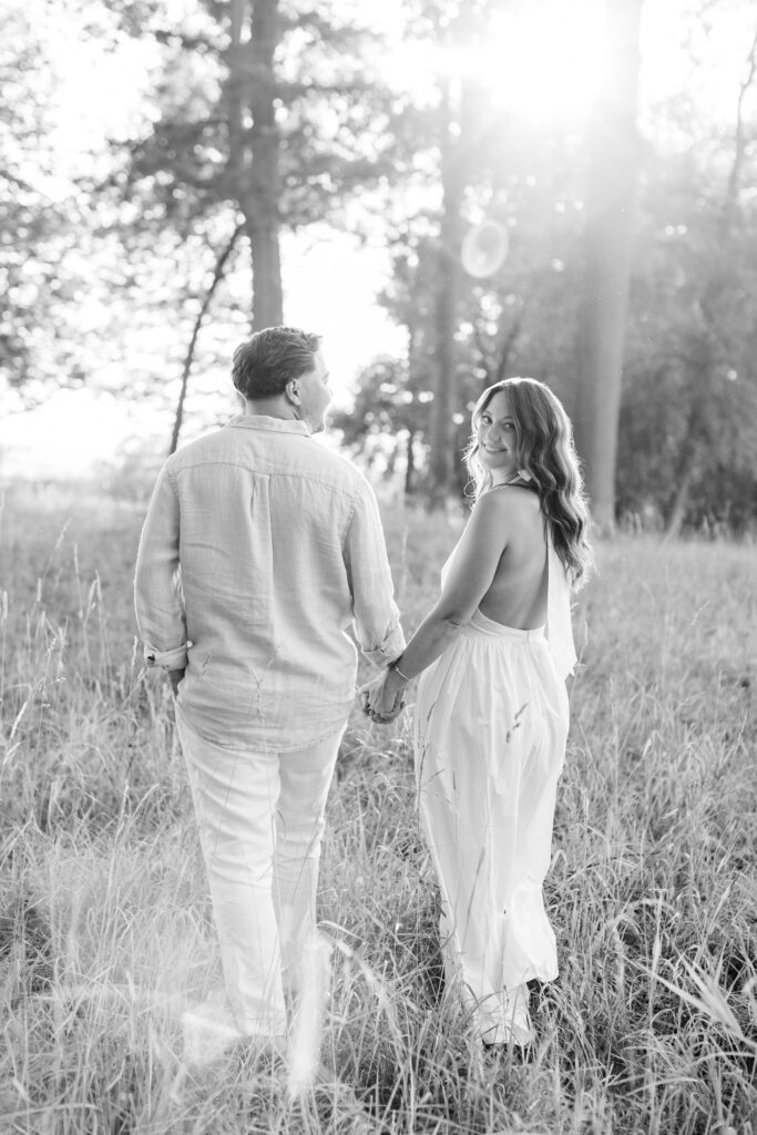 couple holding hands and walking into the sunlight during their engagement session