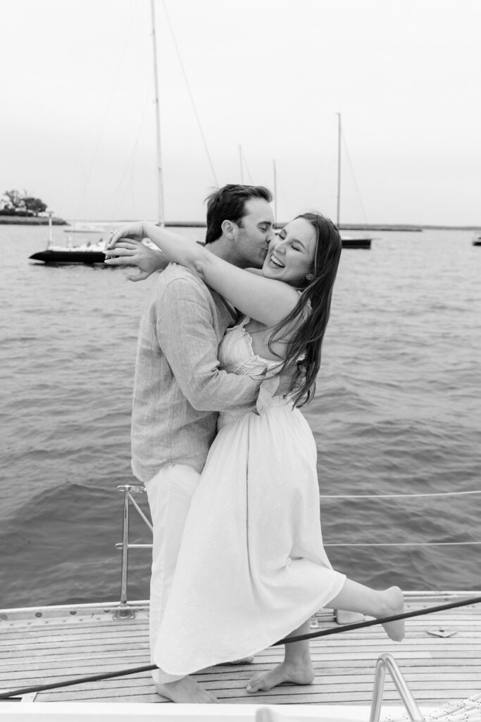 couple laughing and kissing on the sailboat during their engagement session at Larchmont Yacht Club
