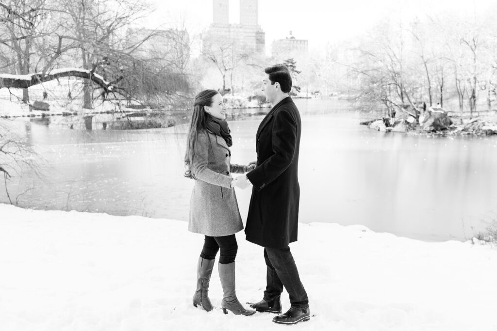 black and white photo of couple laughing in a snowy field in Central Park during engagement session