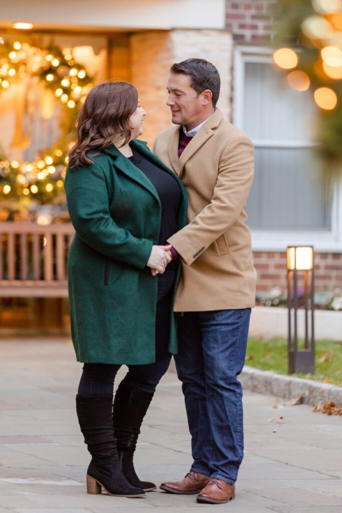 couple surrounded by Christmas lights holding hands during winter engagement session in New York