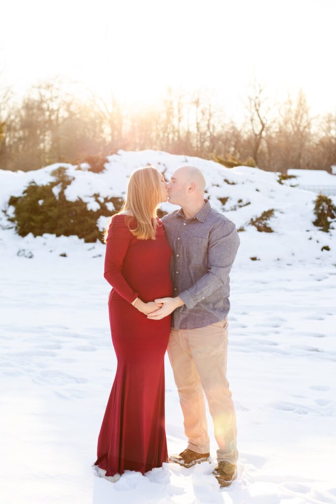 couple kissing and holding hands during engagement session in snowy field at Harts Brook Park and Preserve in NY