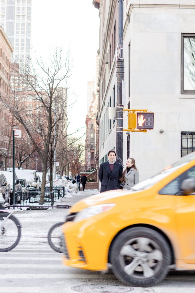 couple waiting to cross the street with a NYC taxi cab crossing in the foreground