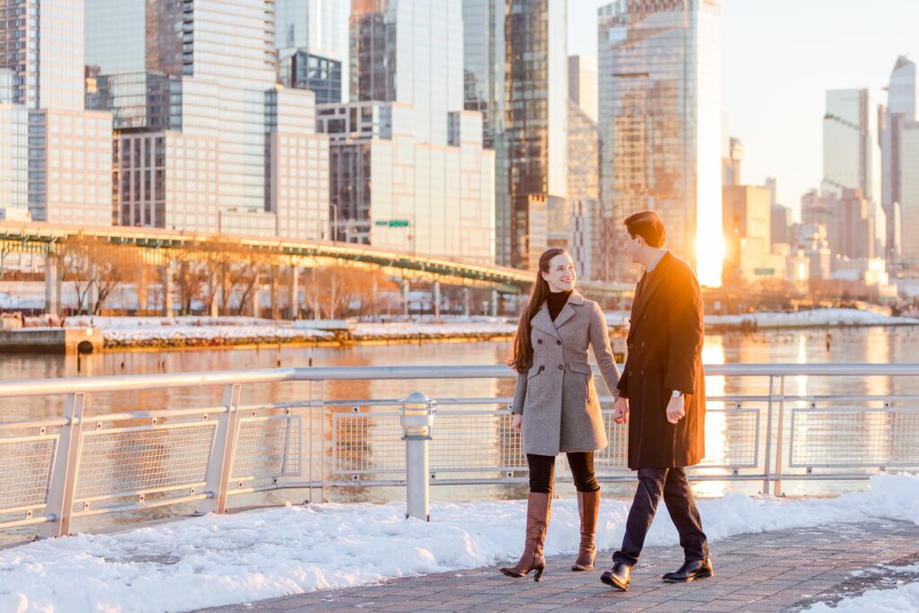 couple walking in the sunset on the snowy Pier 1 with NYC in the background during winter engagement session